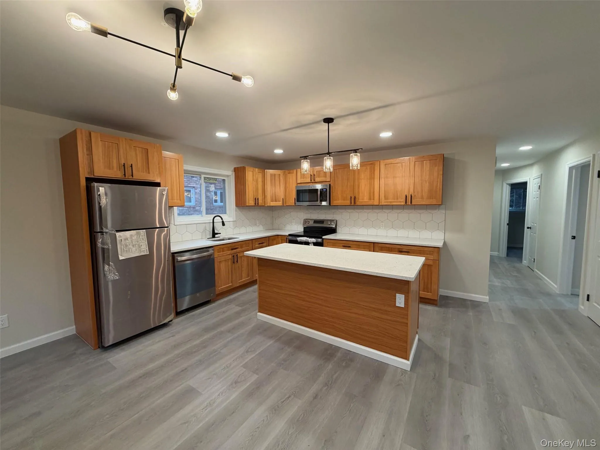 Kitchen with appliances with stainless steel finishes, decorative light fixtures, backsplash, a center island, and brown cabinetry Kitchen with appliances with stainless steel finishes, decorative light fixtures, backsplash, a center island, and brown cabinetry
