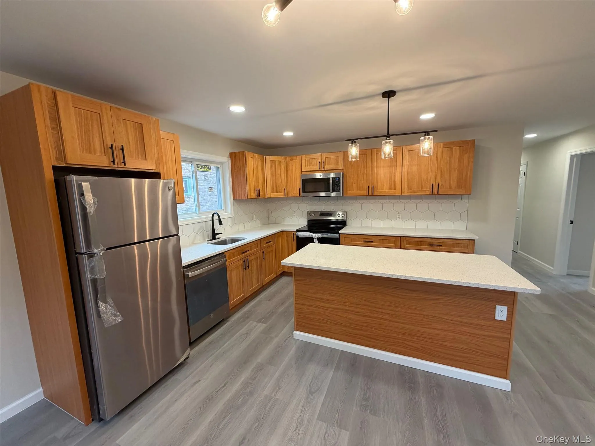 Kitchen with appliances with stainless steel finishes, light stone countertops, hanging light fixtures, brown cabinets, and backsplash Kitchen with appliances with stainless steel finishes, light stone countertops, hanging light fixtures, brown cabinets, and backsplash