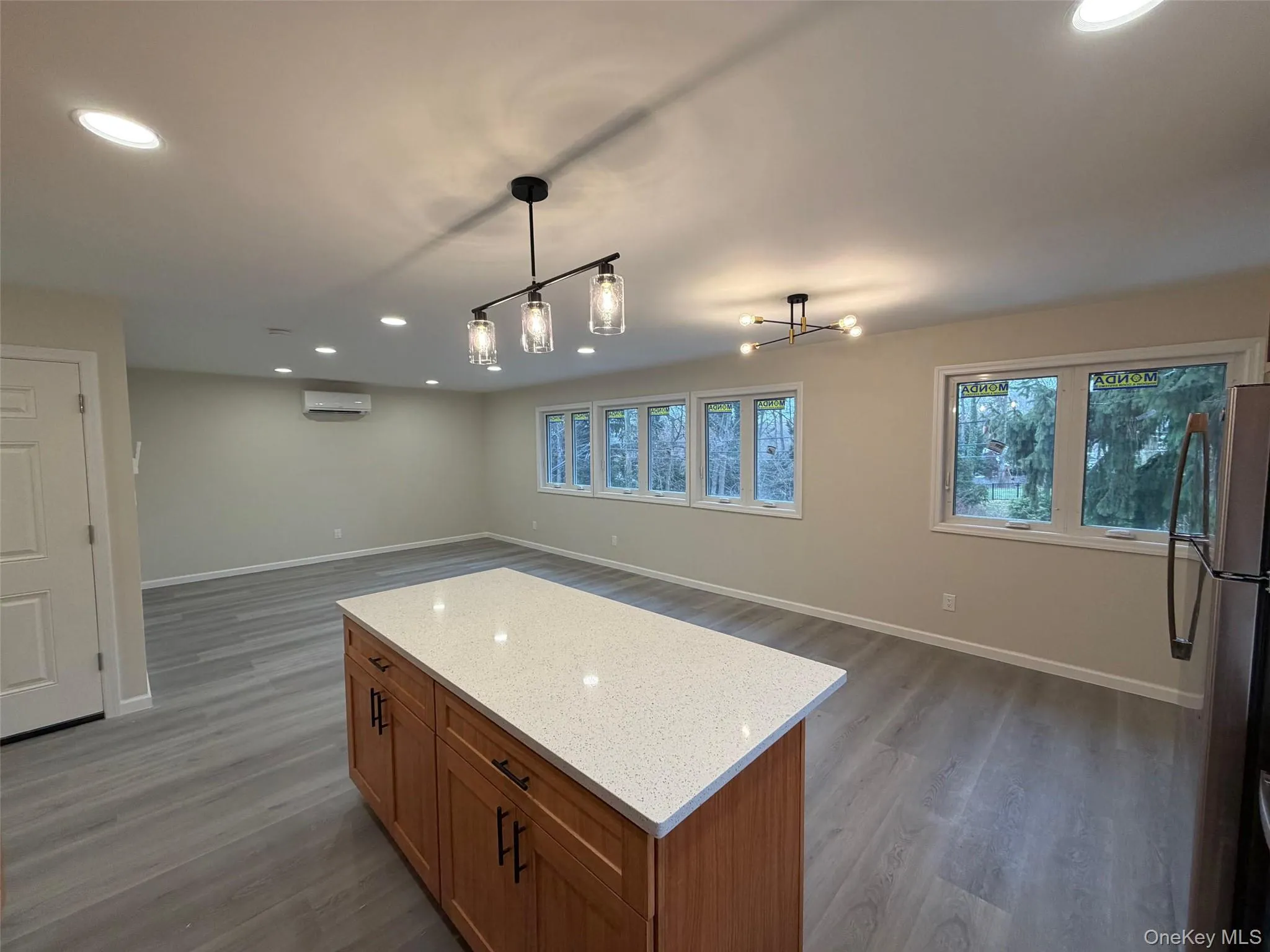 Kitchen with recessed lighting, brown cabinetry, open floor plan, freestanding refrigerator, and a kitchen island Kitchen with recessed lighting, brown cabinetry, open floor plan, freestanding refrigerator, and a kitchen island