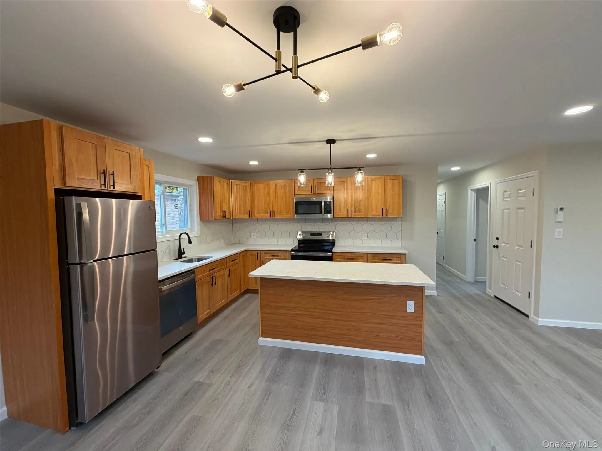 Kitchen with appliances with stainless steel finishes, a center island, light wood-type flooring, brown cabinets, and recessed lighting Kitchen with appliances with stainless steel finishes, a center island, light wood-type flooring, brown cabinets, and recessed lighting