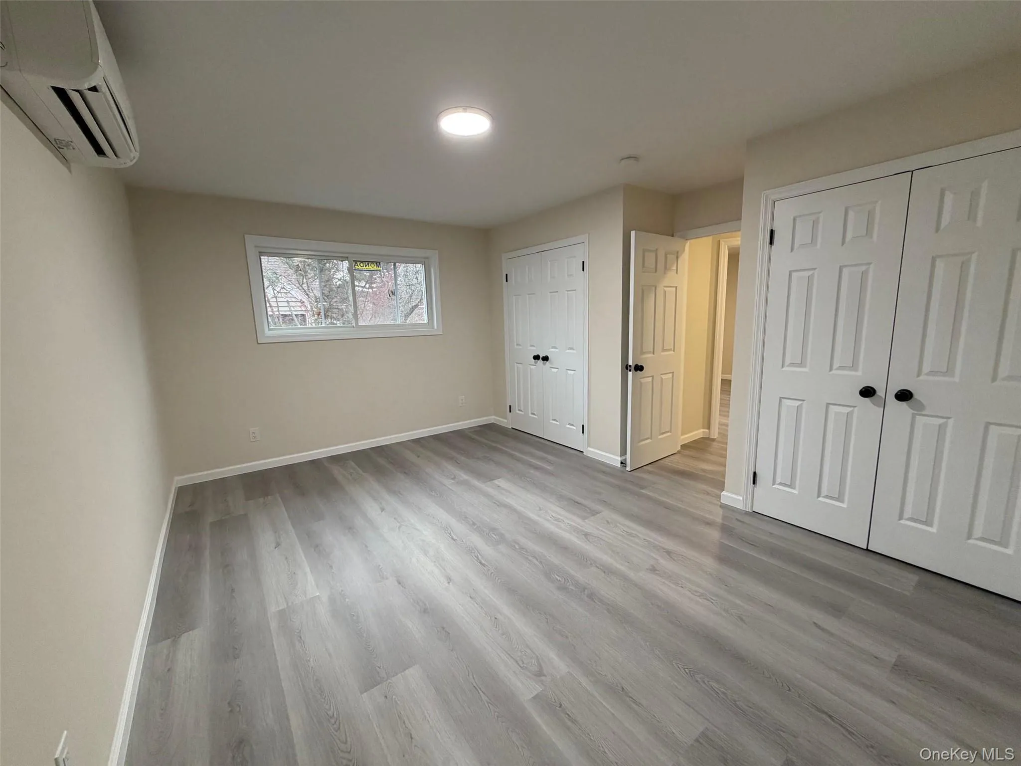 Unfurnished bedroom with a wall unit AC, two closets, and light wood-style flooring Unfurnished bedroom with a wall unit AC, two closets, and light wood-style flooring