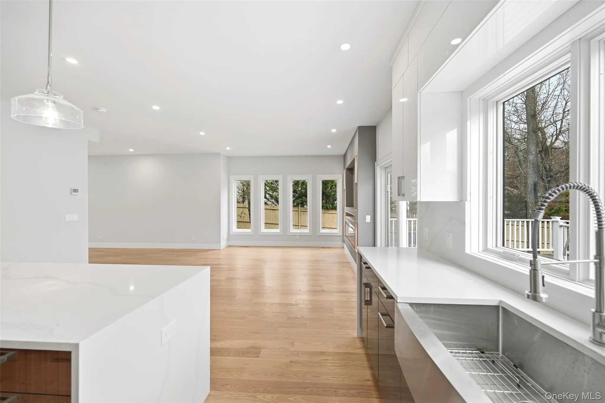 Kitchen with white cabinets, light wood-type flooring, hanging light fixtures, light stone countertops, and recessed lighting Kitchen with white cabinets, light wood-type flooring, hanging light fixtures, light stone countertops, and recessed lighting