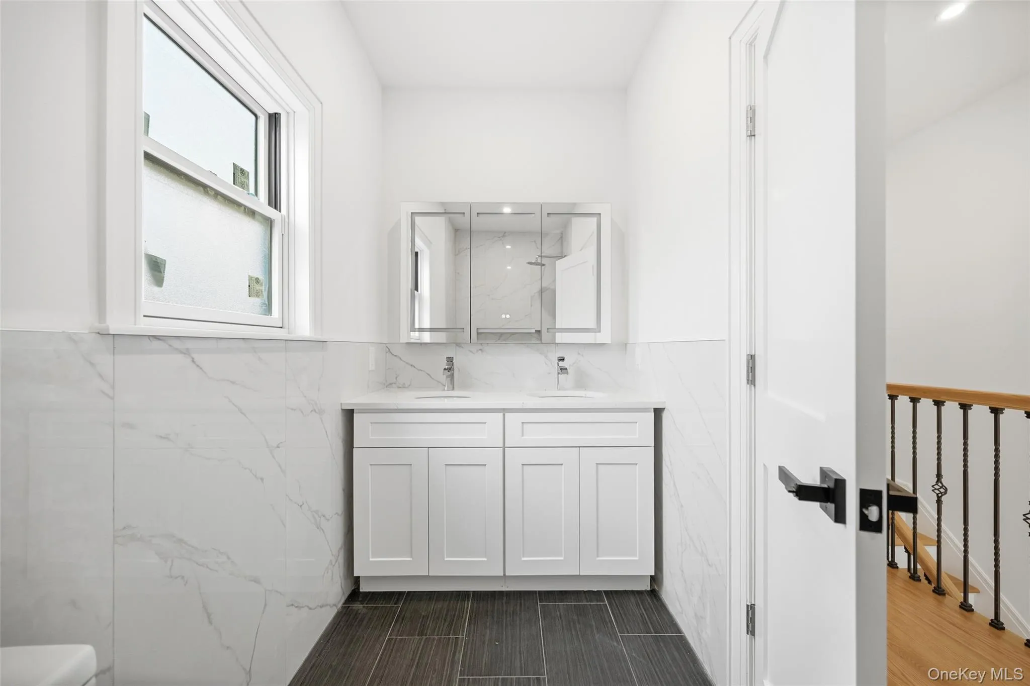 Full bath with double vanity, a marble finish shower, tile walls, and wainscoting Full bath with double vanity, a marble finish shower, tile walls, and wainscoting