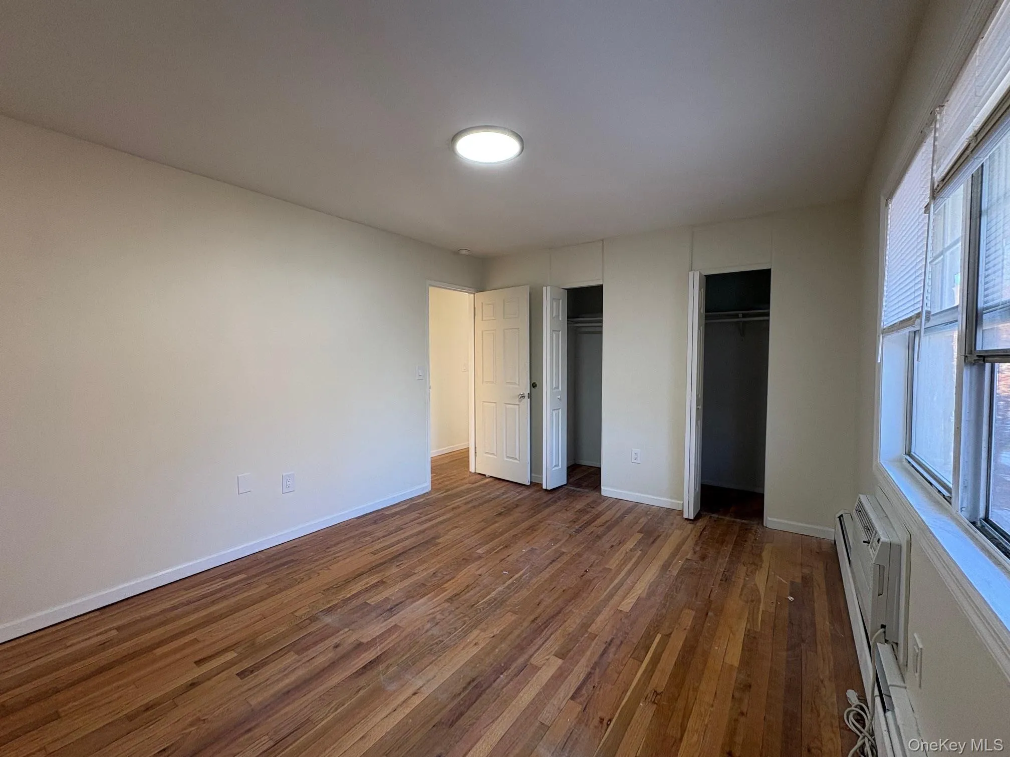 Primary bedroom featuring double closets, wood floors, wall mounted AC Primary bedroom featuring double closets, wood floors, wall mounted AC