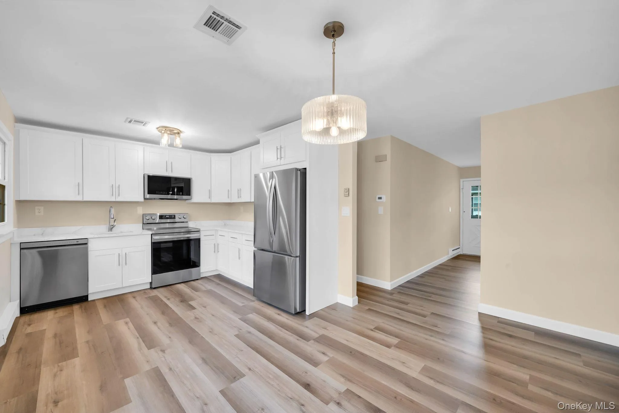 Kitchen featuring stainless steel appliances, white cabinets, a chandelier, and light wood finished floors Kitchen featuring stainless steel appliances, white cabinets, a chandelier, and light wood finished floors