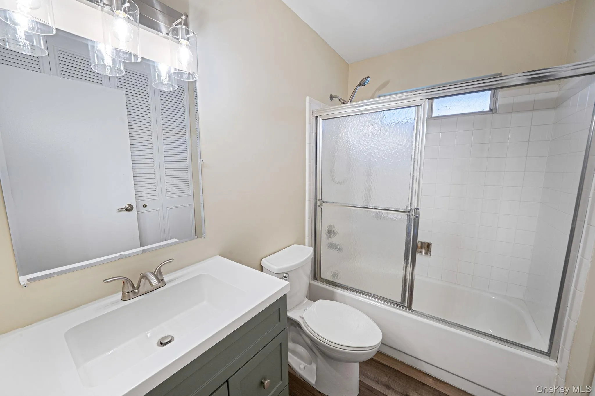 Bathroom featuring vanity, bath / shower combo with glass door, and dark wood-type flooring Bathroom featuring vanity, bath / shower combo with glass door, and dark wood-type flooring