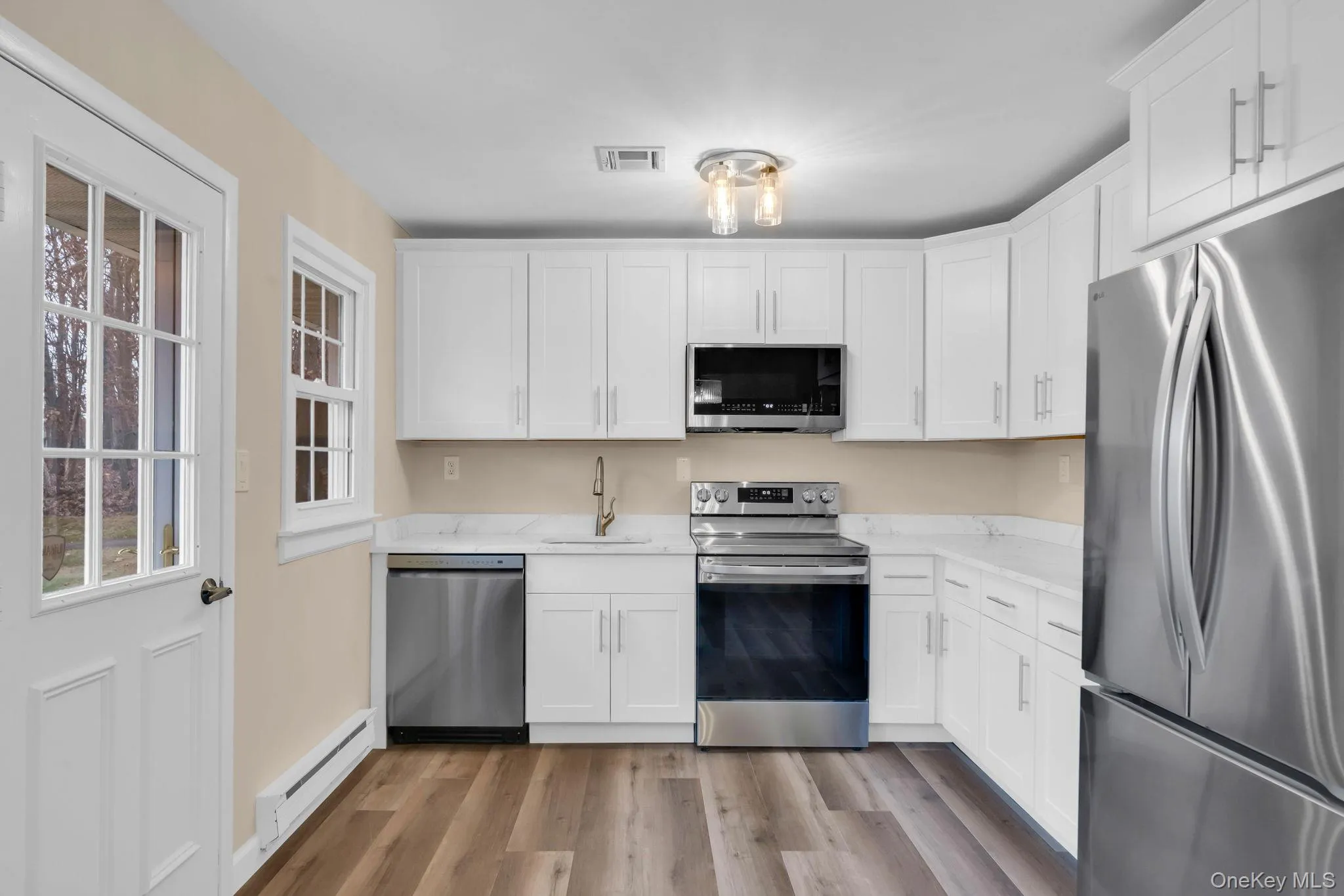 Kitchen featuring appliances with stainless steel finishes, white cabinetry, a baseboard radiator, and light wood-style flooring Kitchen featuring appliances with stainless steel finishes, white cabinetry, a baseboard radiator, and light wood-style flooring