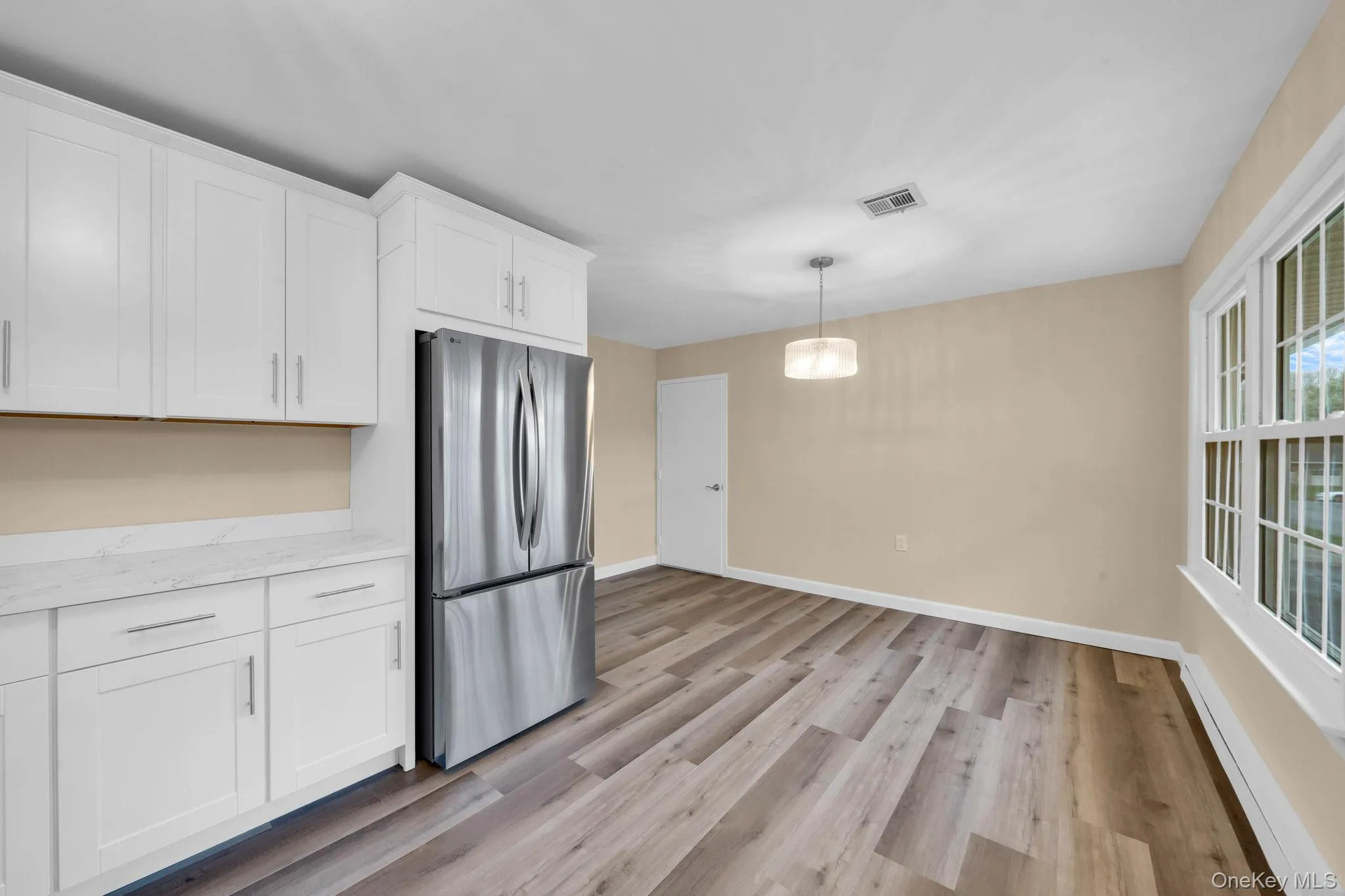 Kitchen with a baseboard radiator, white cabinetry, freestanding refrigerator, light wood-style flooring, and decorative light fixtures Kitchen with a baseboard radiator, white cabinetry, freestanding refrigerator, light wood-style flooring, and decorative light fixtures