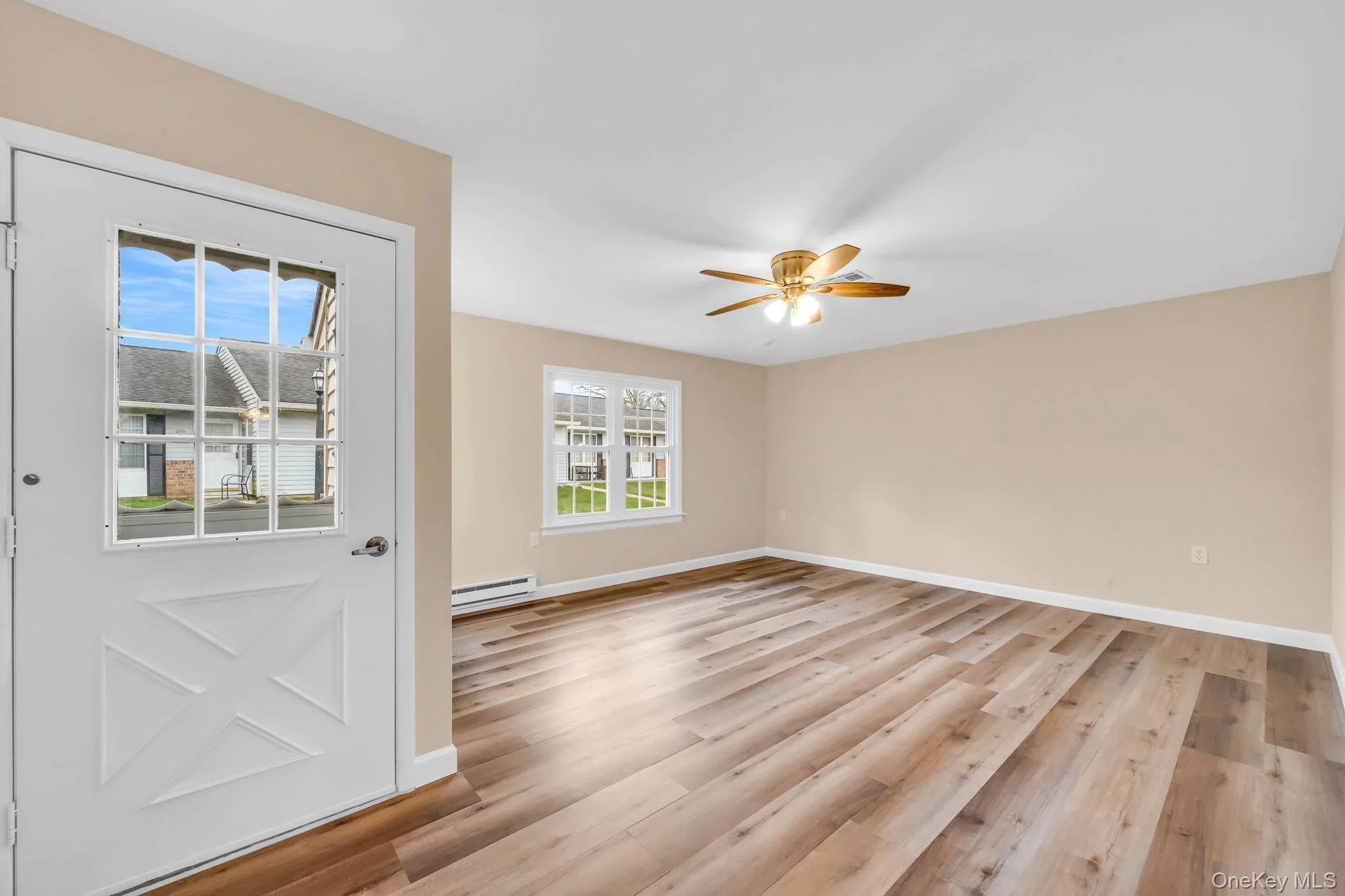 Empty room with light wood-type flooring, a baseboard heating unit, and a ceiling fan Empty room with light wood-type flooring, a baseboard heating unit, and a ceiling fan