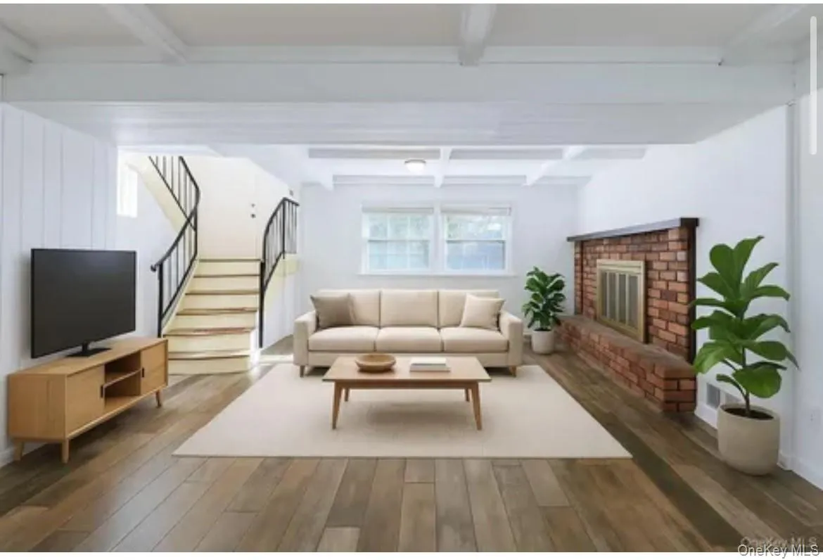Living room featuring wood finished floors, beamed ceiling, stairs, and a brick fireplace Living room featuring wood finished floors, beamed ceiling, stairs, and a brick fireplace