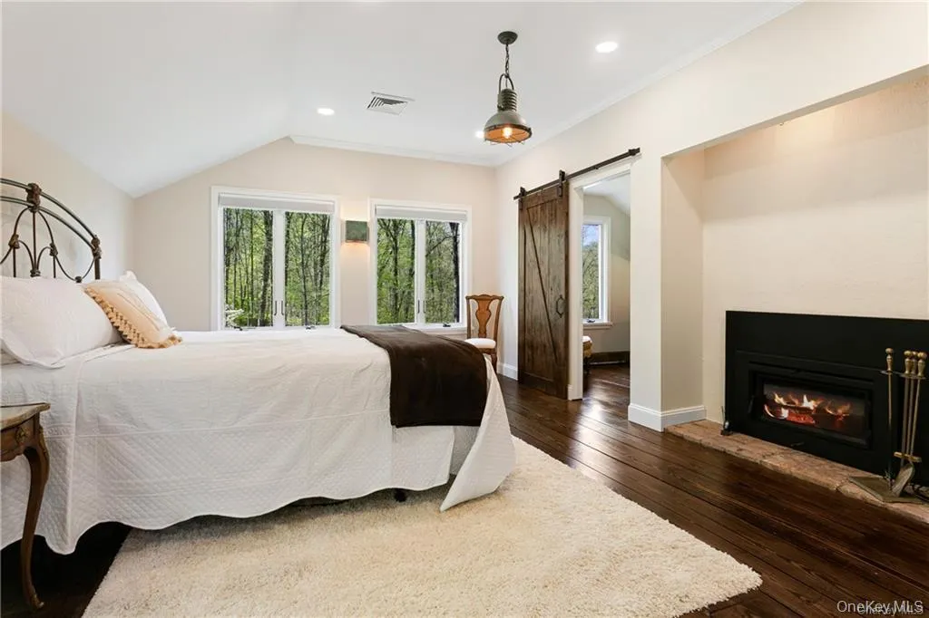 Bedroom with a barn door, dark wood-style flooring, recessed lighting, ornamental molding, and a glass covered fireplace Bedroom with a barn door, dark wood-style flooring, recessed lighting, ornamental molding, and a glass covered fireplace