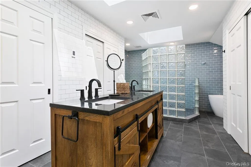 Bathroom with a skylight, double vanity, a freestanding tub, tile walls, and a walk in shower Bathroom with a skylight, double vanity, a freestanding tub, tile walls, and a walk in shower
