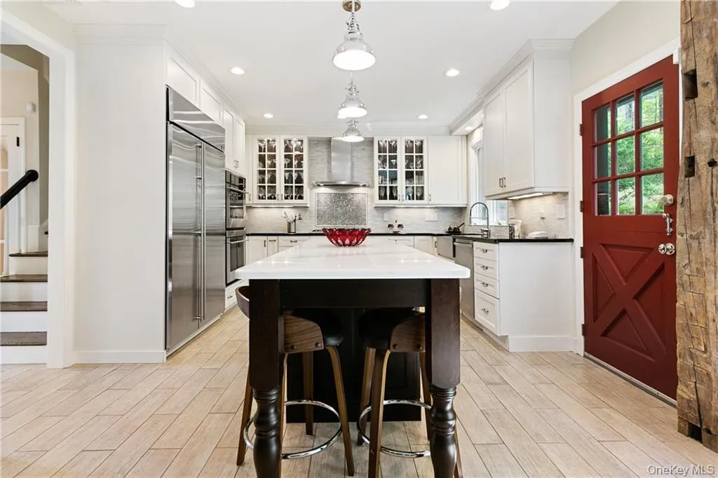 Kitchen featuring hanging light fixtures, a center island, stainless steel appliances, white cabinetry, and dark stone countertops Kitchen featuring hanging light fixtures, a center island, stainless steel appliances, white cabinetry, and dark stone countertops