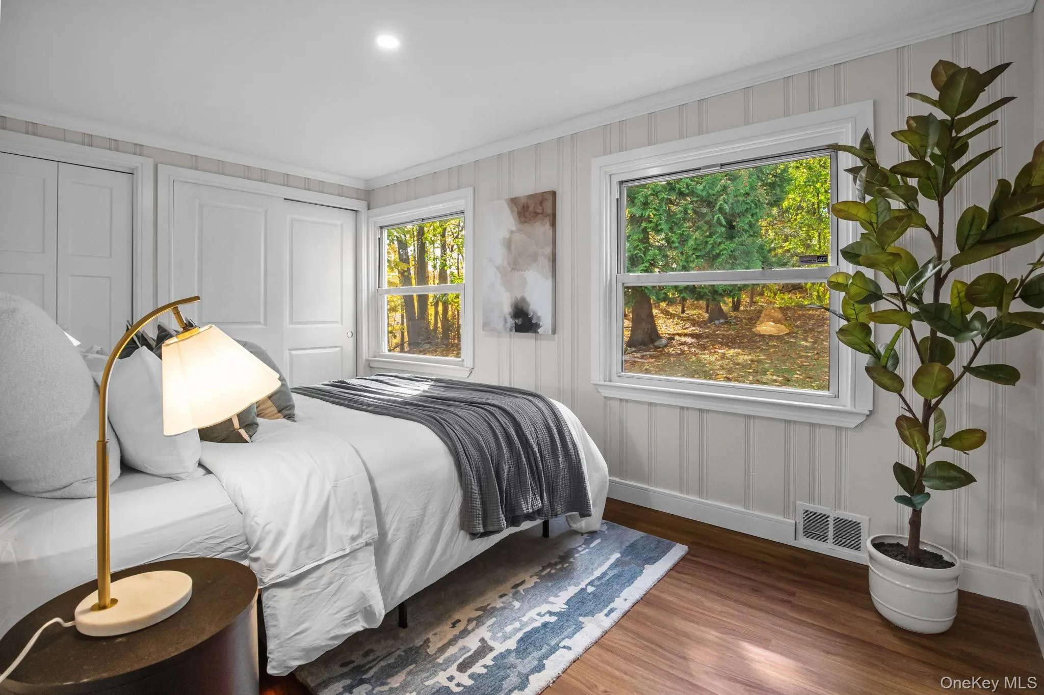 Newly renovated bedroom with warm hardwood floors and picture windows framing serene wooded views for a peaceful retreat. Newly renovated bedroom with warm hardwood floors and picture windows framing serene wooded views for a peaceful retreat.