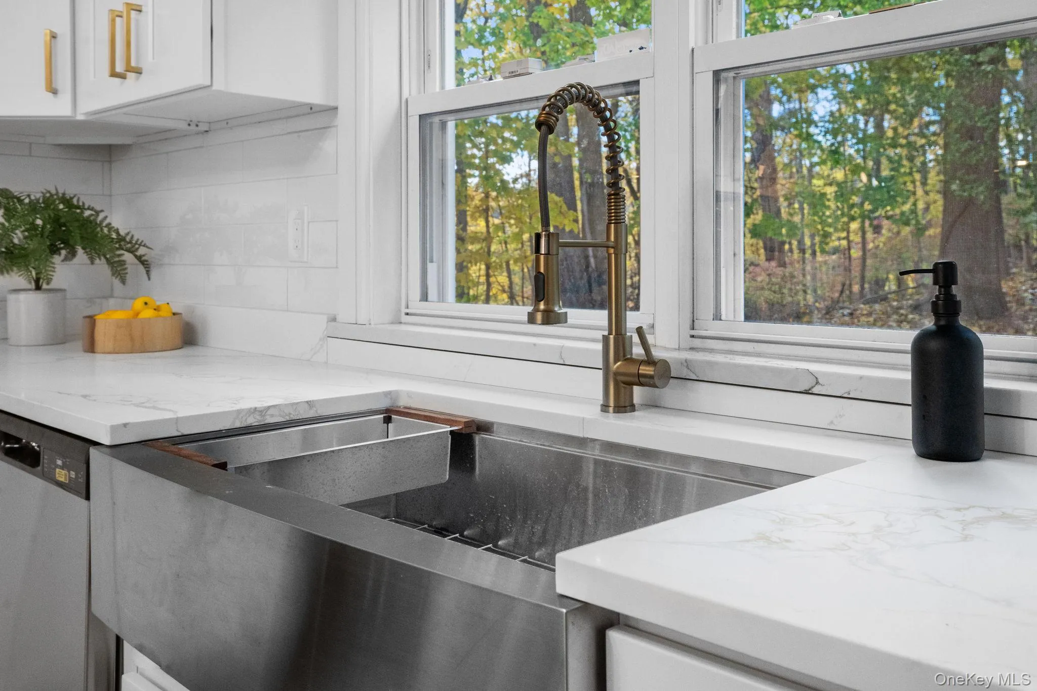 Stylish farmhouse sink with brass faucet and quartz countertops overlooks the private backyard, adding beauty to everyday routines. Stylish farmhouse sink with brass faucet and quartz countertops overlooks the private backyard, adding beauty to everyday routines.