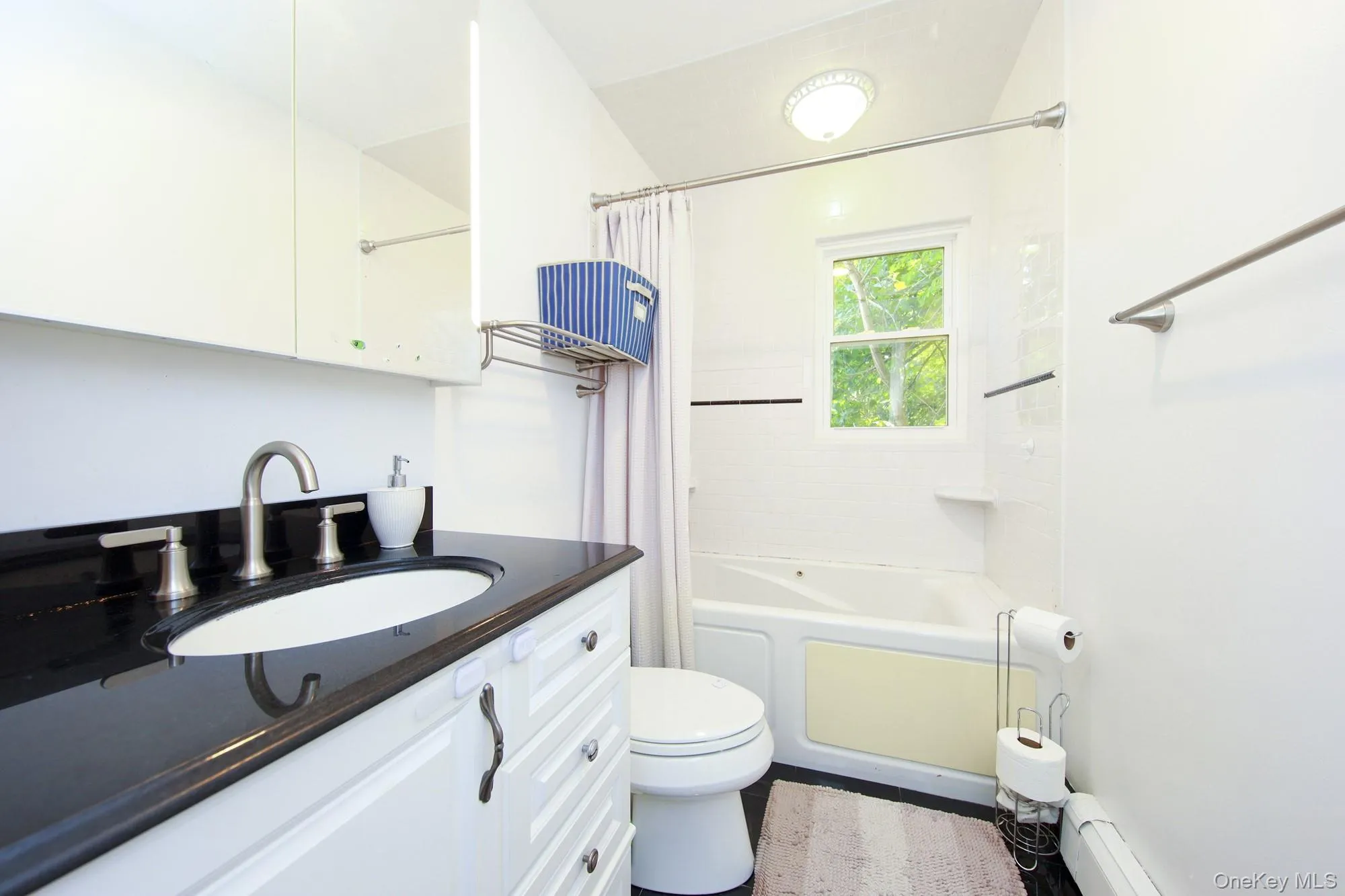 Full bathroom featuring vanity, a baseboard heating unit, and shower / bathtub combination with curtain Full bathroom featuring vanity, a baseboard heating unit, and shower / bathtub combination with curtain