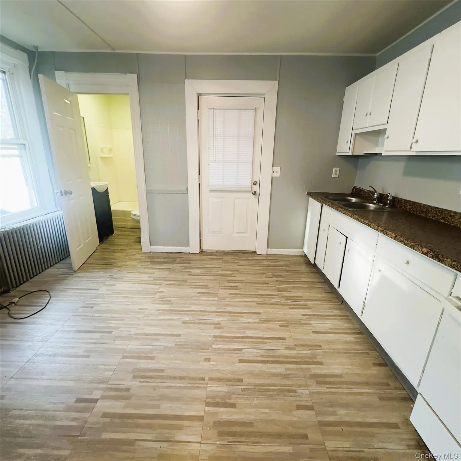 Kitchen featuring white cabinetry, radiator heating unit, and light fixture, vinyl flooring, radiator. Kitchen featuring white cabinetry, radiator heating unit, and light fixture, vinyl flooring, radiator.