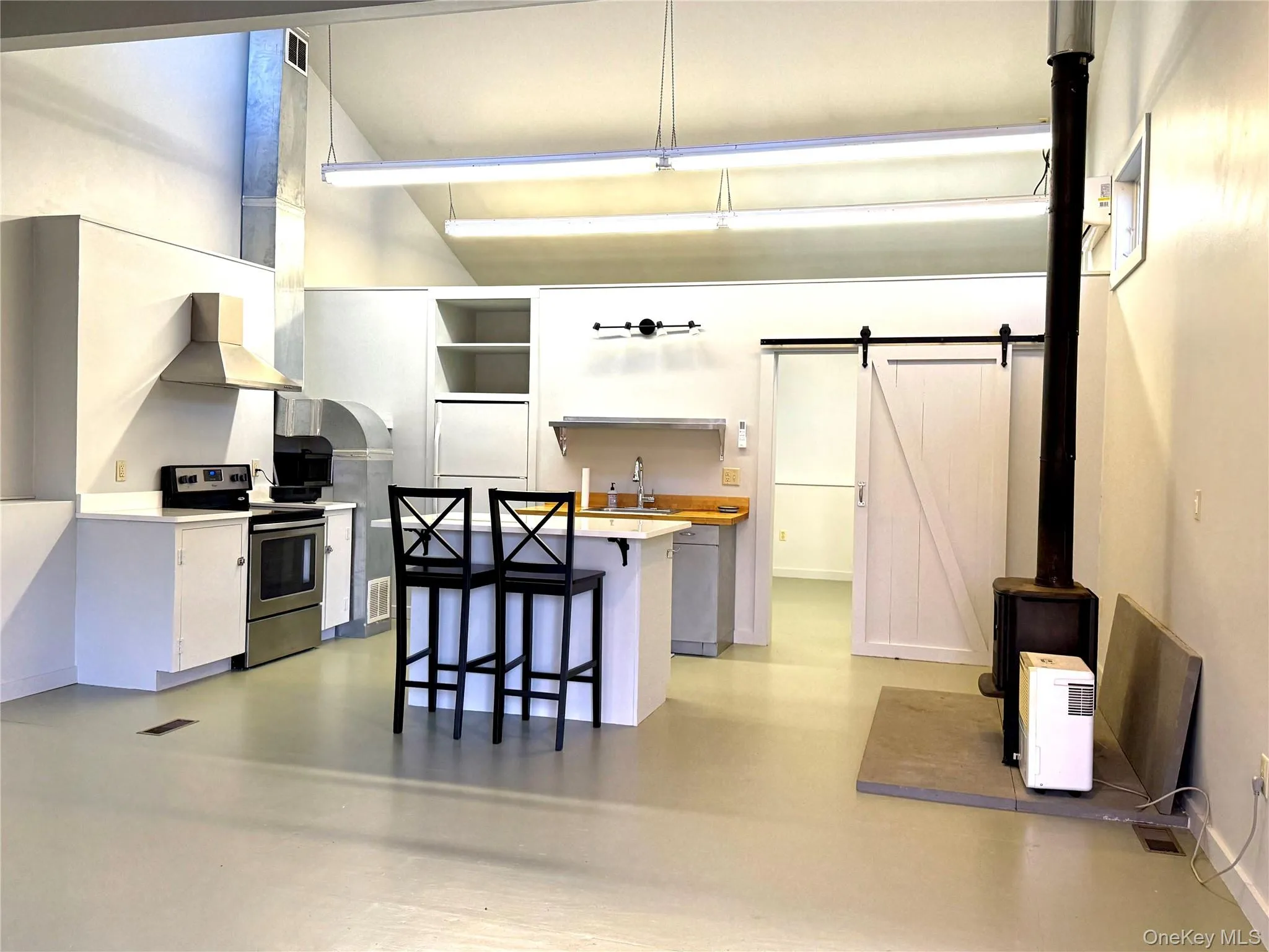 Kitchen featuring light countertops, electric stove, white cabinetry, a breakfast bar, and wall chimney exhaust hood Kitchen featuring light countertops, electric stove, white cabinetry, a breakfast bar, and wall chimney exhaust hood