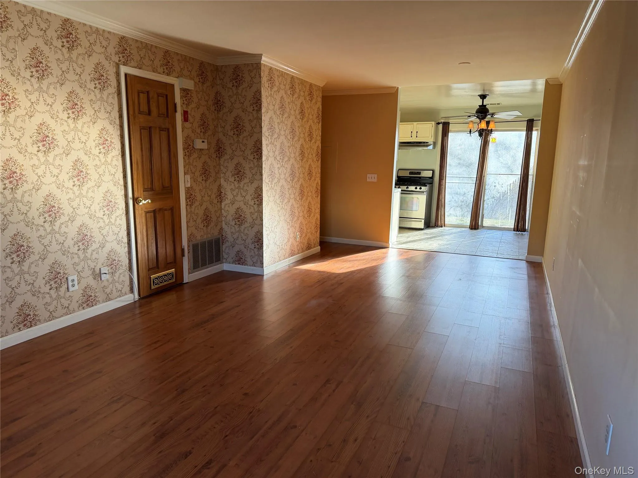 Unfurnished room featuring dark wood-style floors, ceiling fan, wallpapered walls, and crown molding Unfurnished room featuring dark wood-style floors, ceiling fan, wallpapered walls, and crown molding