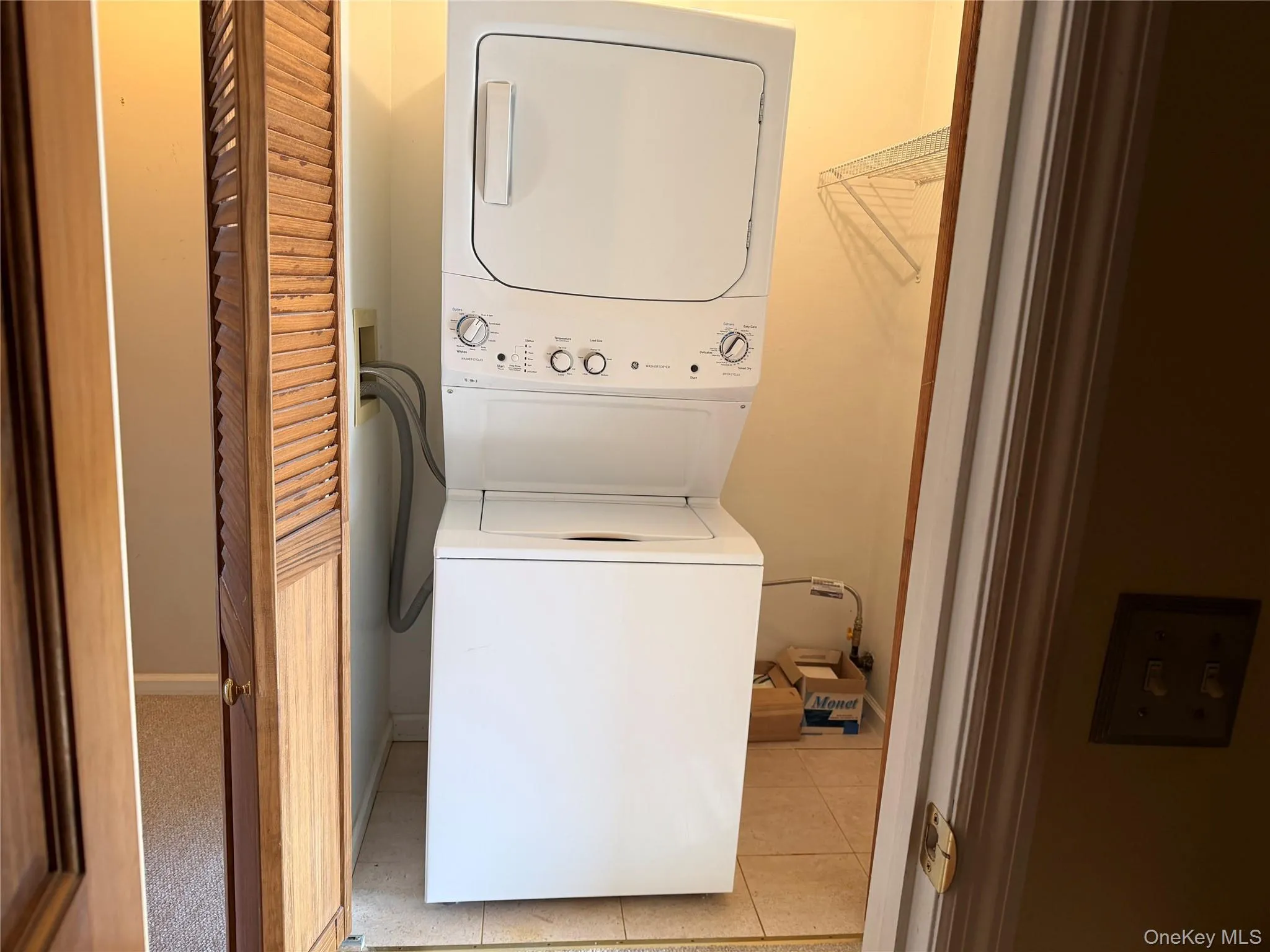 Laundry area with stacked washer / drying machine and light tile patterned floors Laundry area with stacked washer / drying machine and light tile patterned floors