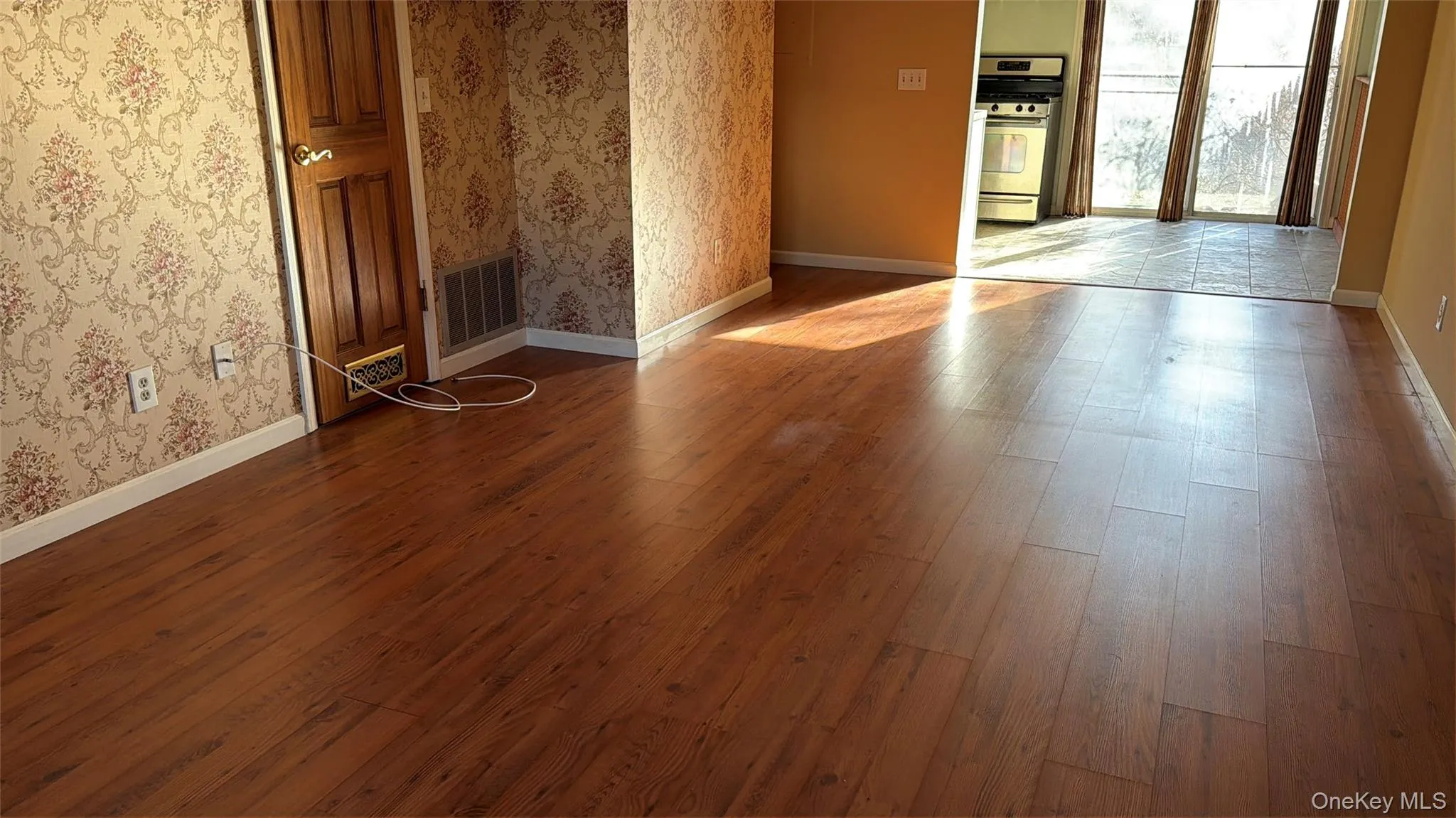 Spare room with wallpapered walls and dark wood-style flooring Spare room with wallpapered walls and dark wood-style flooring