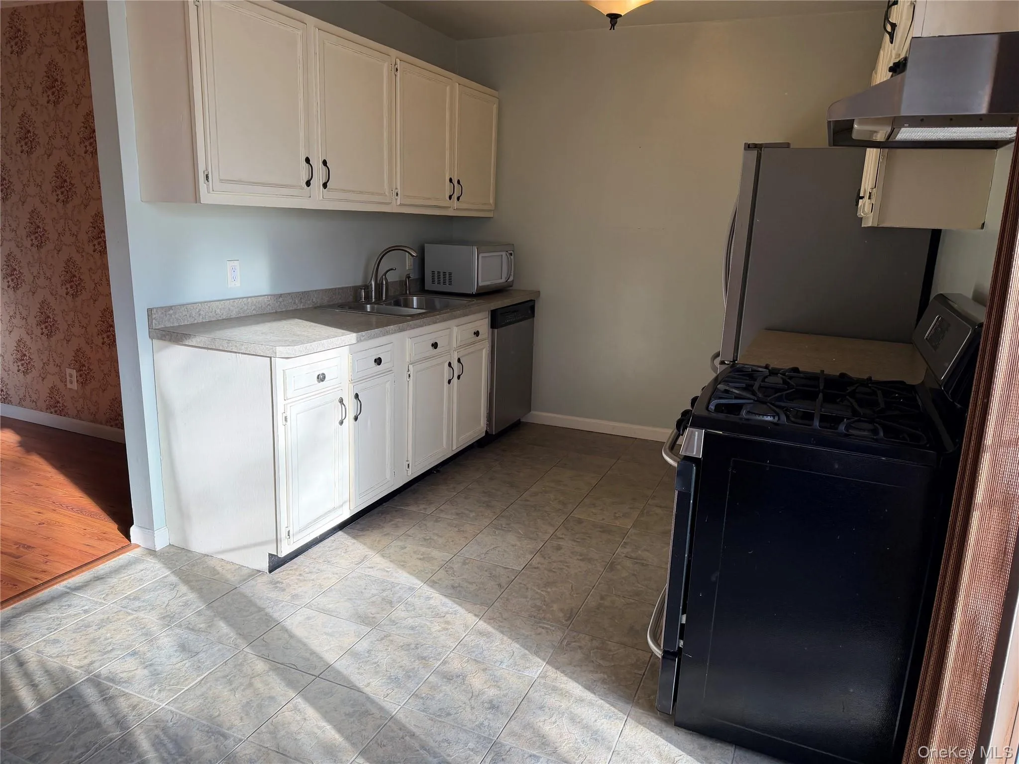 Kitchen with appliances with stainless steel finishes, white cabinetry, light countertops, and under cabinet range hood Kitchen with appliances with stainless steel finishes, white cabinetry, light countertops, and under cabinet range hood