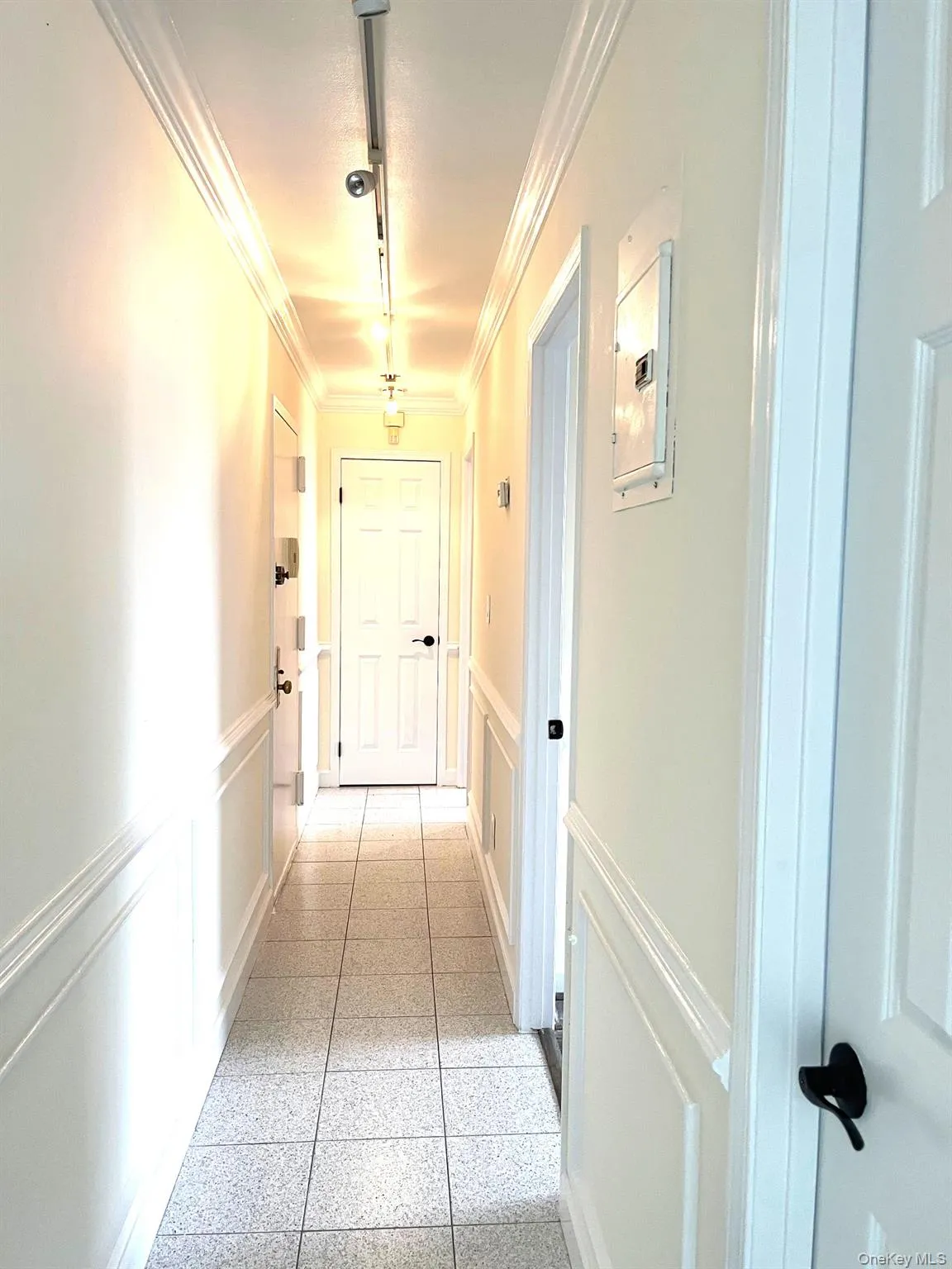 Corridor with track lighting, a decorative wall, ornamental molding, and wainscoting Corridor with track lighting, a decorative wall, ornamental molding, and wainscoting