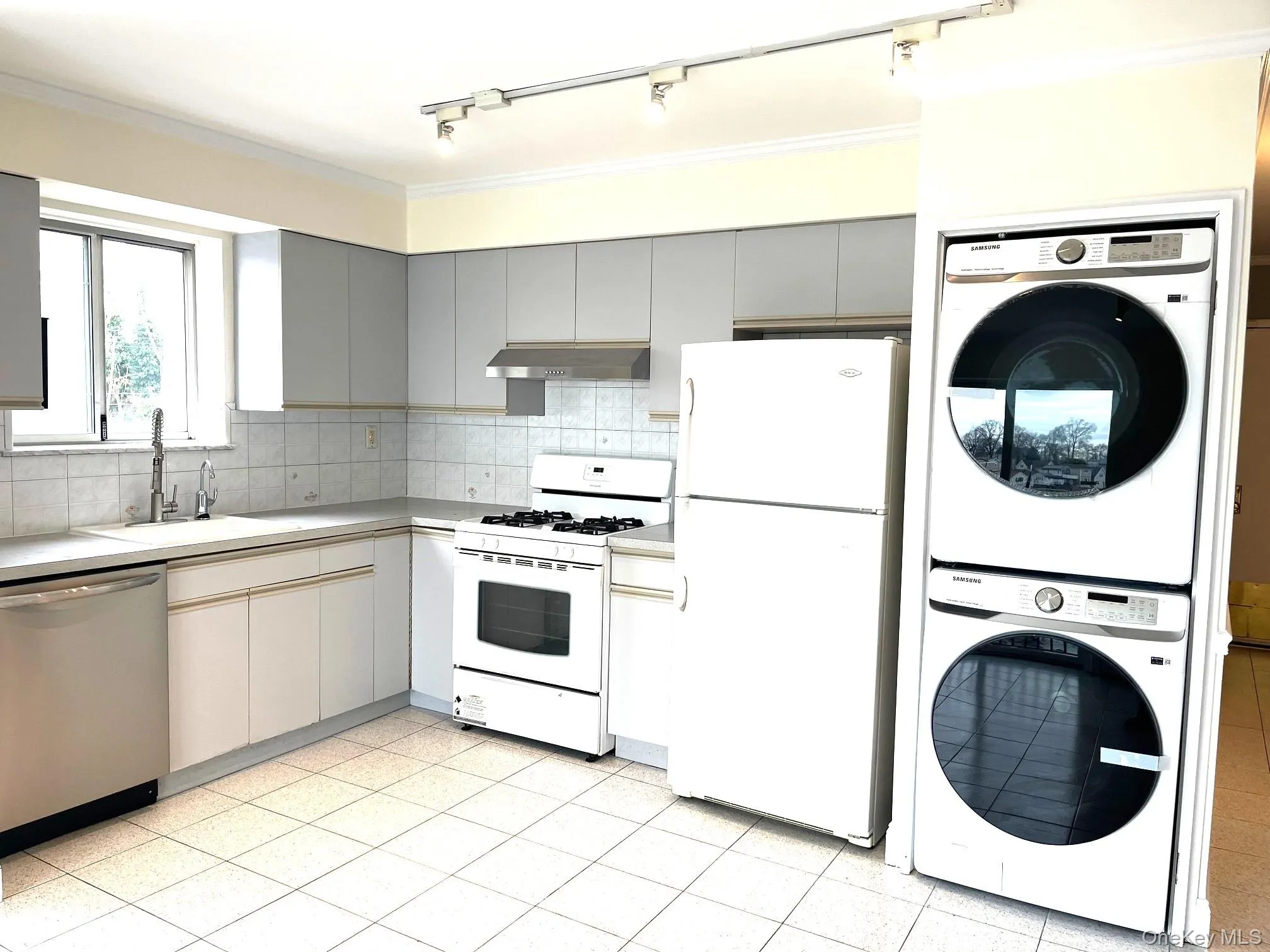 Kitchen featuring white appliances, estacked washer and dryer, light countertops, under cabinet range hood, and tasteful backsplash Kitchen featuring white appliances, estacked washer and dryer, light countertops, under cabinet range hood, and tasteful backsplash