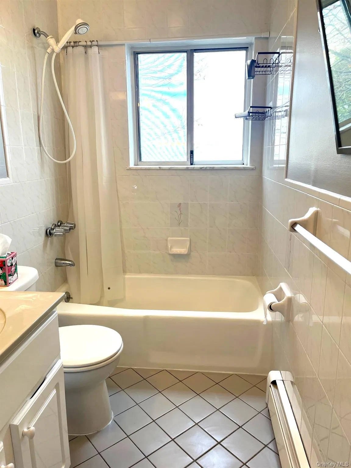 Bathroom with shower / tub combo, vanity, a baseboard heating unit, light tile patterned floors, and tile walls Bathroom with shower / tub combo, vanity, a baseboard heating unit, light tile patterned floors, and tile walls