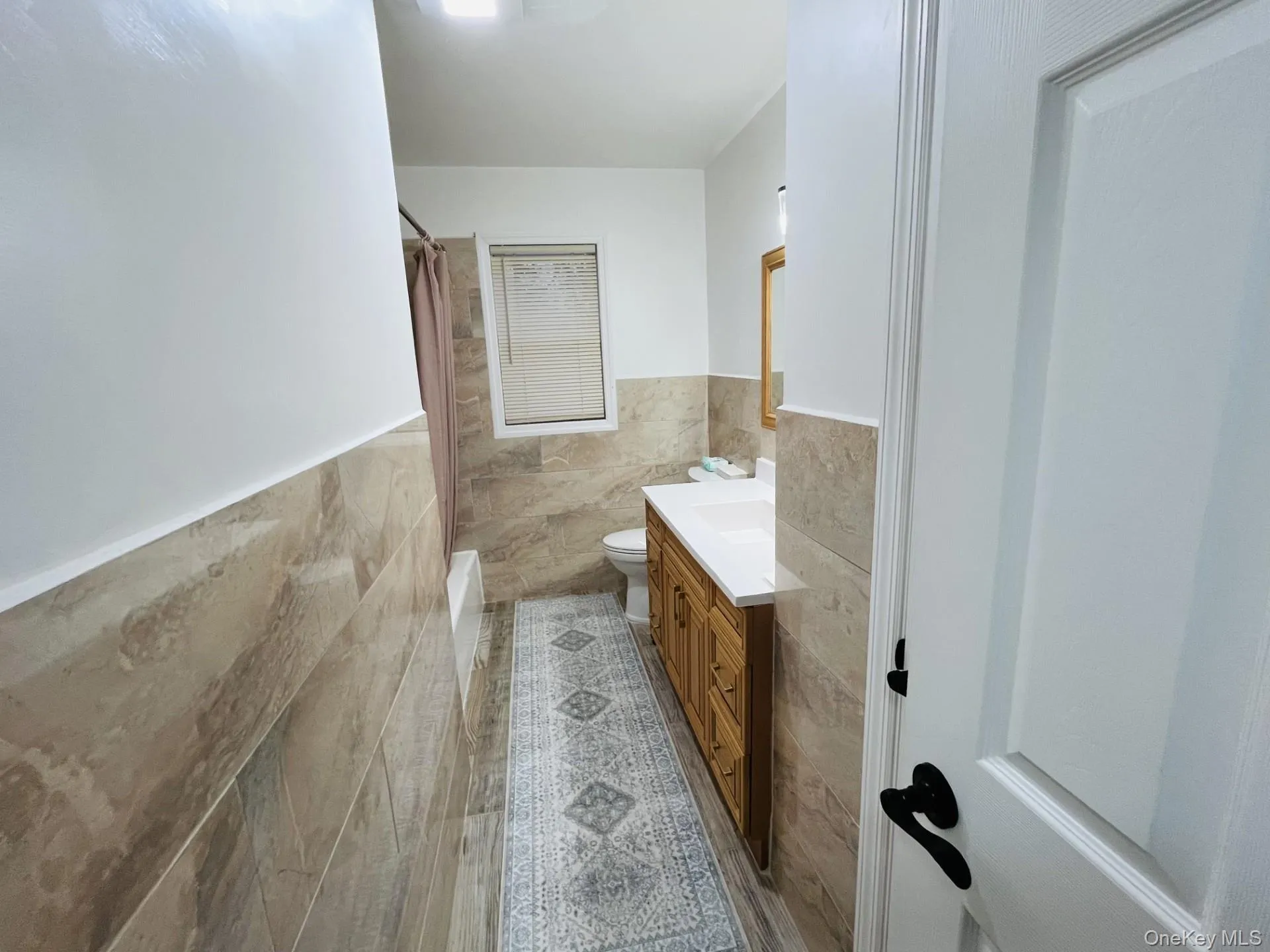 Bathroom with tile walls, vanity, a wainscoted wall, and shower / bath combo Bathroom with tile walls, vanity, a wainscoted wall, and shower / bath combo