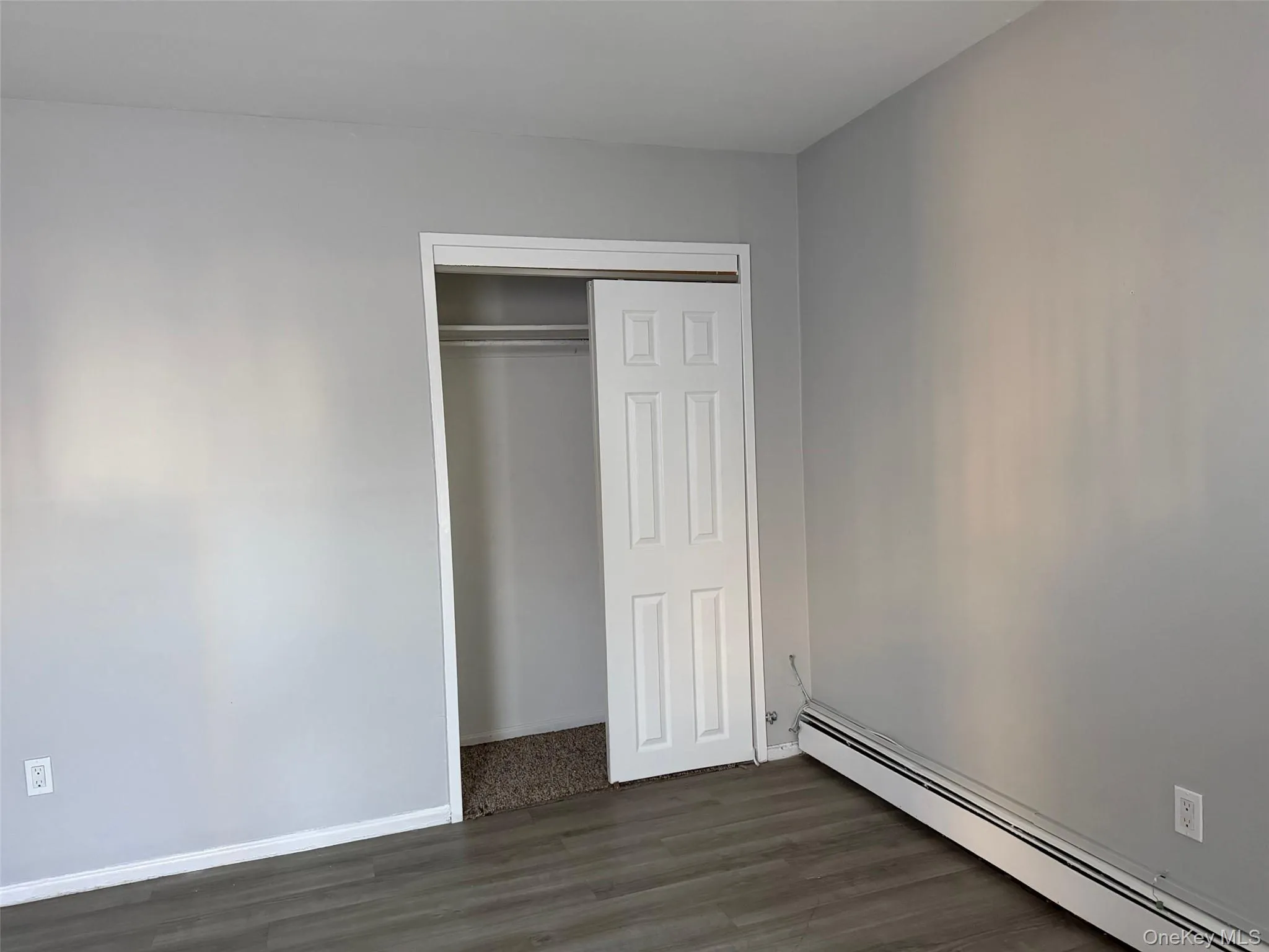 Unfurnished bedroom featuring a baseboard radiator, dark wood-style flooring, and a closet Unfurnished bedroom featuring a baseboard radiator, dark wood-style flooring, and a closet