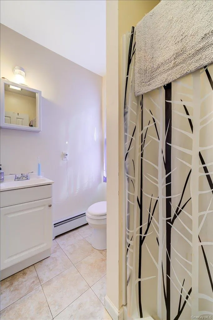 Full bath with vanity, a shower with curtain, a baseboard heating unit, and light tile patterned floors Full bath with vanity, a shower with curtain, a baseboard heating unit, and light tile patterned floors