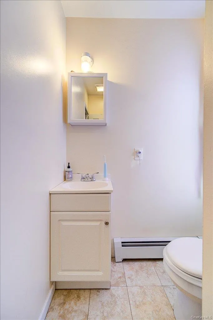 Bathroom featuring vanity, a baseboard heating unit, and light tile patterned floors Bathroom featuring vanity, a baseboard heating unit, and light tile patterned floors