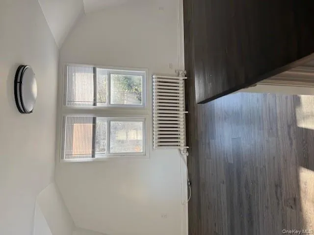 Bonus room featuring vaulted ceiling, radiator heating unit, and dark wood-style flooring Bonus room featuring vaulted ceiling, radiator heating unit, and dark wood-style flooring