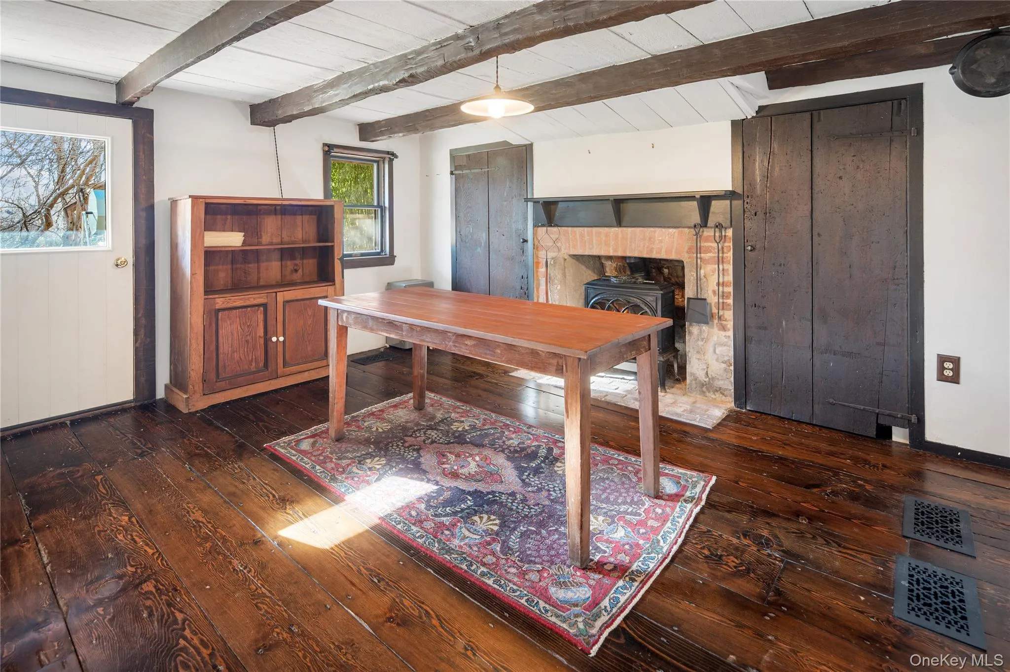 Ground level dining room with beautiful wide plank hardwood flooring, ceiling with exposed beams, and cast iron Jotul wood-burning stove insert in fireplace Ground level dining room with beautiful wide plank hardwood flooring, ceiling with exposed beams, and cast iron Jotul wood-burning stove insert in fireplace