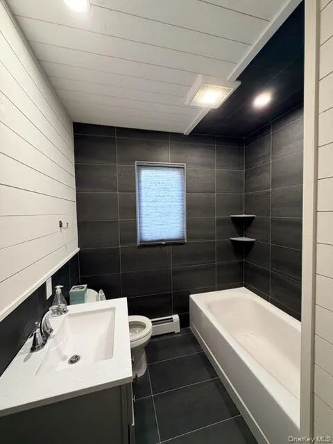 Bathroom featuring dark tile patterned flooring, vanity, and baseboard heating Bathroom featuring dark tile patterned flooring, vanity, and baseboard heating