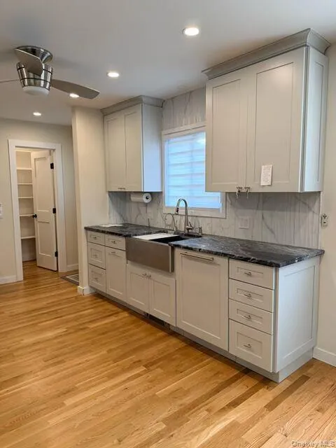 Kitchen with light wood-style floors, dark stone counters, recessed lighting, and backsplash Kitchen with light wood-style floors, dark stone counters, recessed lighting, and backsplash