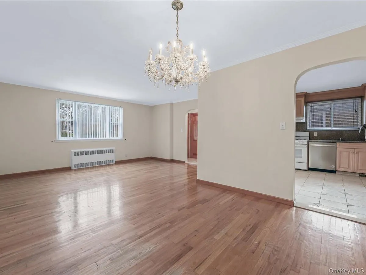Dining room with arched walkways to kitchen, light wood-type flooring, radiator heating unit, and a chandelier Dining room with arched walkways to kitchen, light wood-type flooring, radiator heating unit, and a chandelier