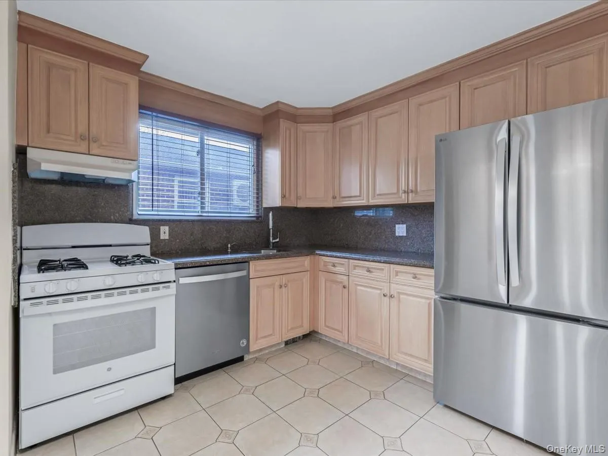 Kitchen with appliances with stainless steel finishes, tasteful backsplash, under cabinet range hood, dark stone countertops, and light brown cabinets Kitchen with appliances with stainless steel finishes, tasteful backsplash, under cabinet range hood, dark stone countertops, and light brown cabinets