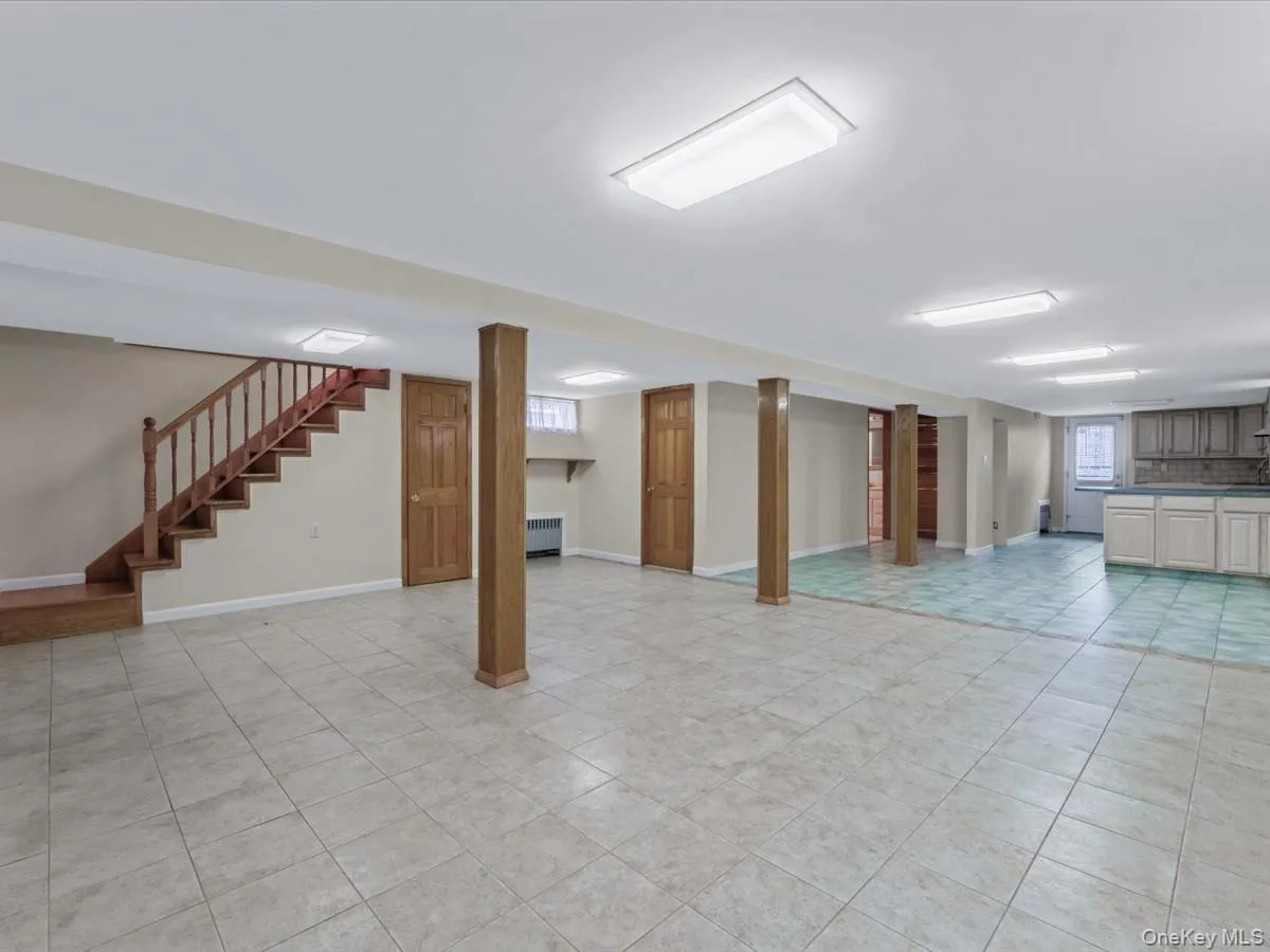Basement featuring stairs, radiator heating unit, and light tile patterned flooring Basement featuring stairs, radiator heating unit, and light tile patterned flooring