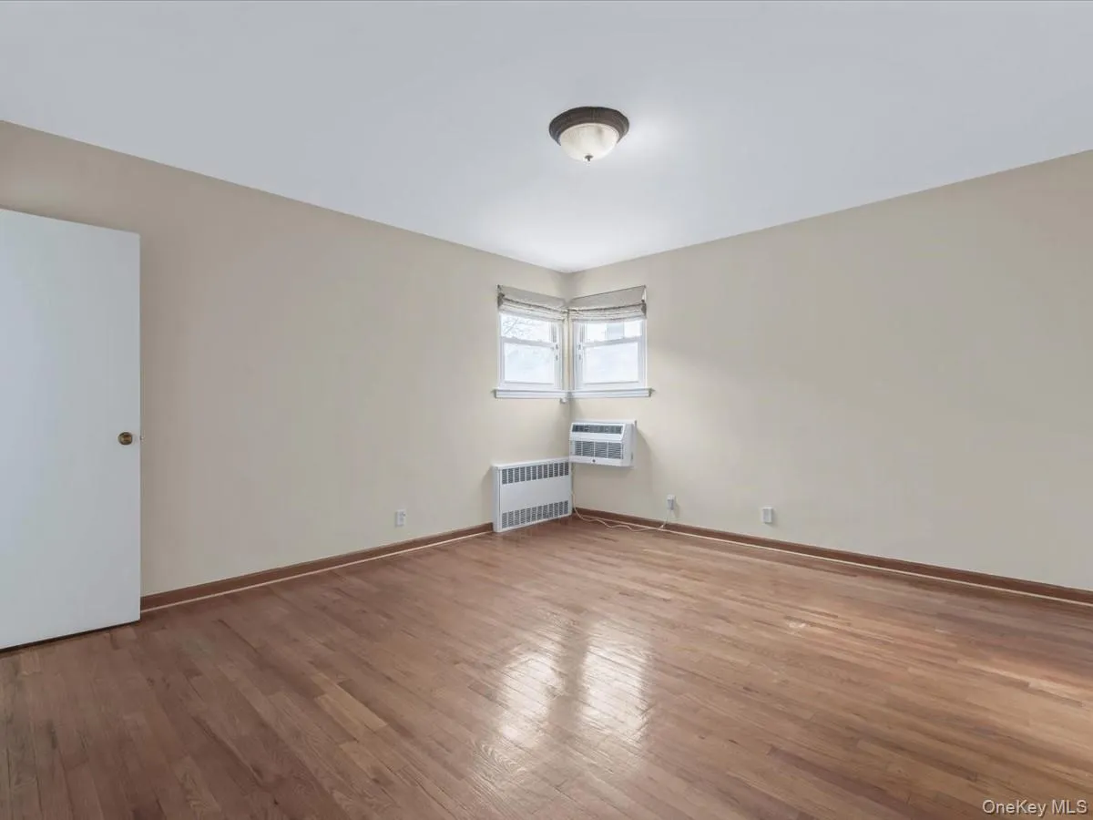 Primary Bedroom featuring light wood-style flooring, radiator heating unit, and a wall unit AC Primary Bedroom featuring light wood-style flooring, radiator heating unit, and a wall unit AC