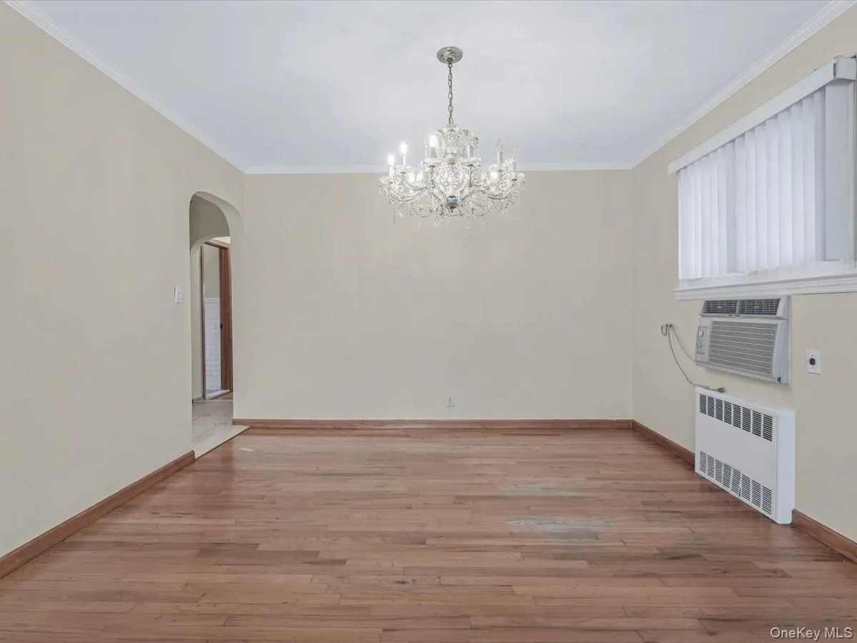 Dining room with light wood-style flooring, radiator heating unit, crown molding, arched walkways, and a chandelier Dining room with light wood-style flooring, radiator heating unit, crown molding, arched walkways, and a chandelier