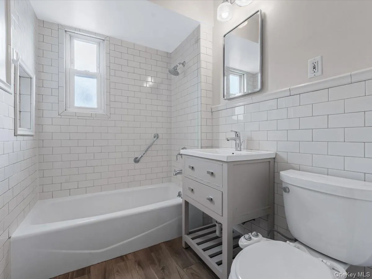 Full bathroom with shower / bath combination, tile walls, vanity, dark wood-type flooring, and a wainscoted wall Full bathroom with shower / bath combination, tile walls, vanity, dark wood-type flooring, and a wainscoted wall