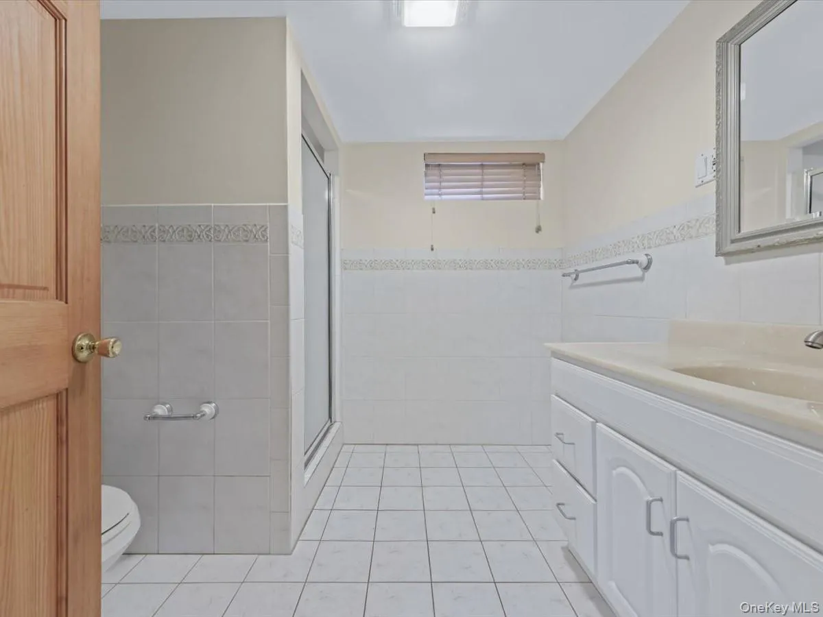 Basement Bathroom featuring vanity, light tile patterned flooring, a shower stall, tile walls, and a wainscoted wall Basement Bathroom featuring vanity, light tile patterned flooring, a shower stall, tile walls, and a wainscoted wall