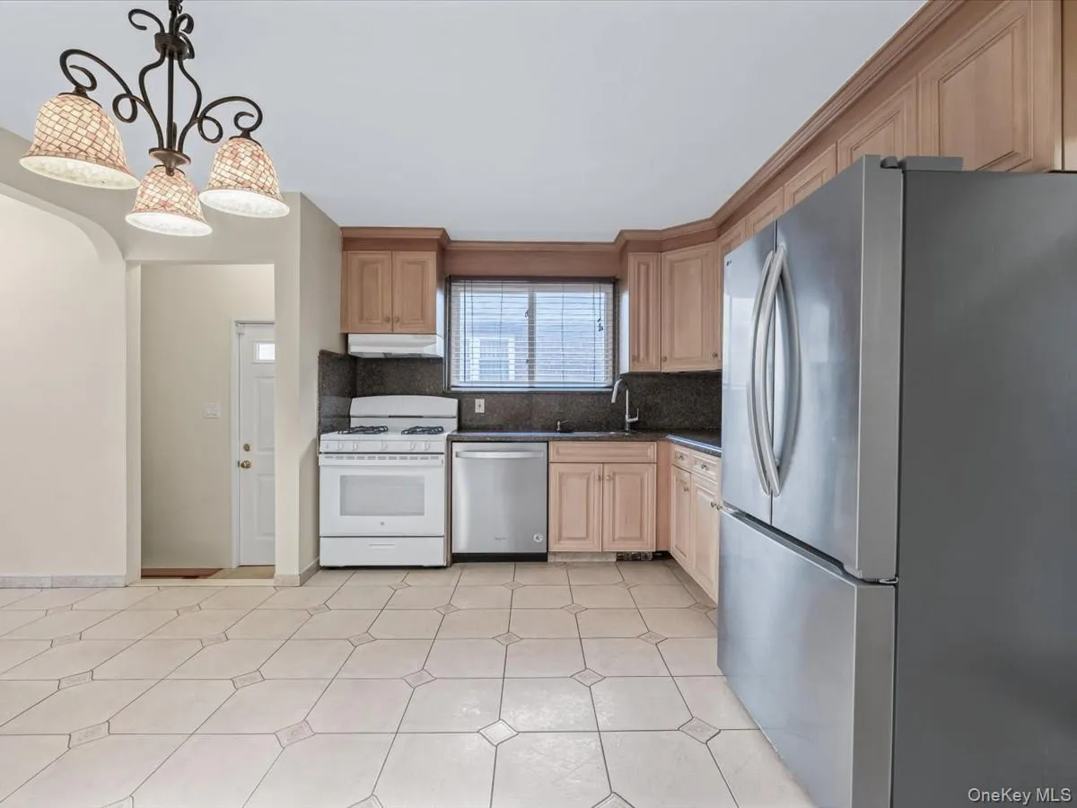 Kitchen featuring appliances with stainless steel finishes, decorative light fixtures, tasteful backsplash, under cabinet range hood, and light brown cabinets Kitchen featuring appliances with stainless steel finishes, decorative light fixtures, tasteful backsplash, under cabinet range hood, and light brown cabinets