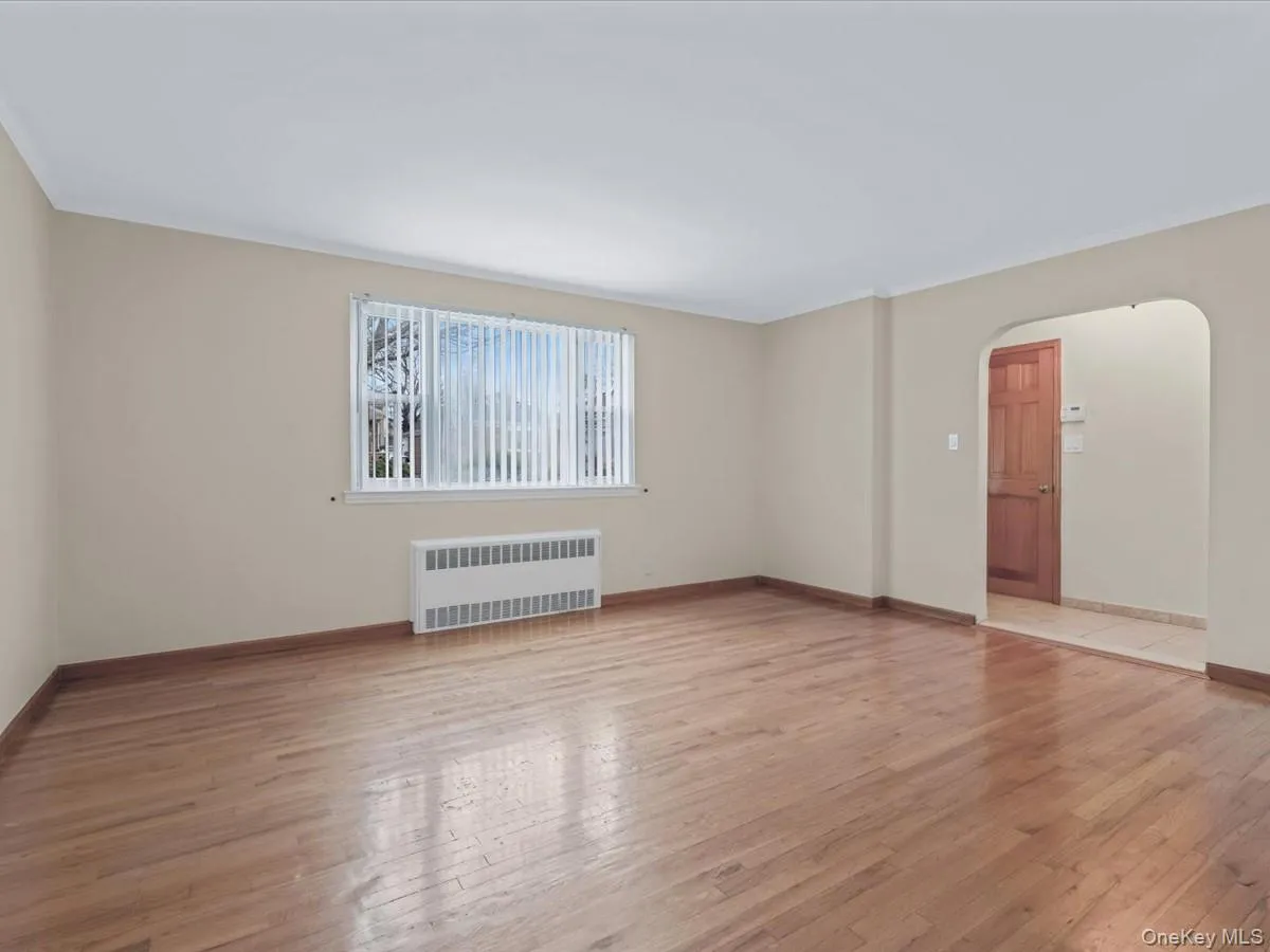 Living room featuring light wood-type flooring, arched walkways, radiator heating unit, and crown molding Living room featuring light wood-type flooring, arched walkways, radiator heating unit, and crown molding