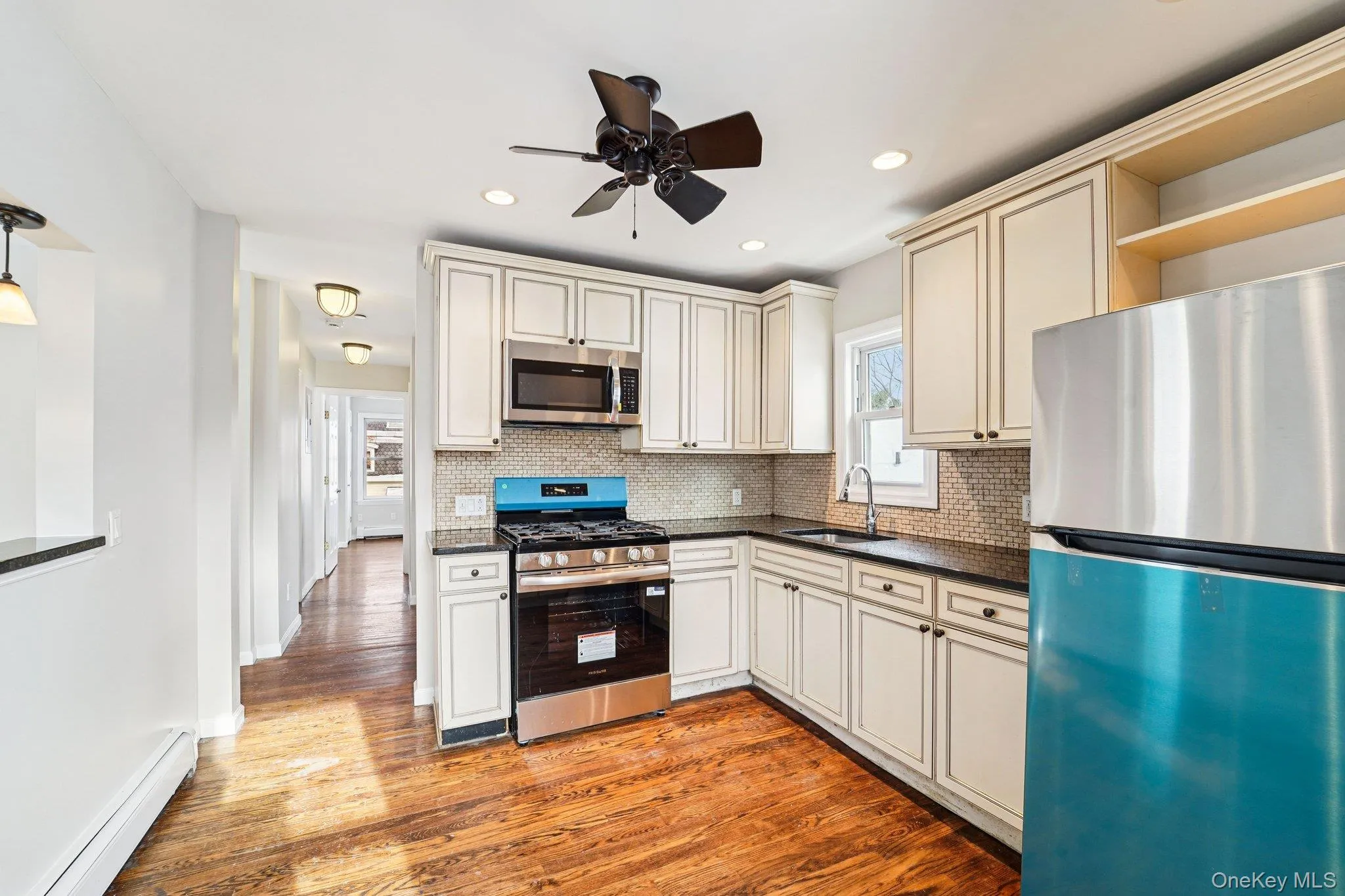 Kitchen with stainless steel appliances, open shelves, a baseboard radiator, light wood-style flooring, and a ceiling fan Kitchen with stainless steel appliances, open shelves, a baseboard radiator, light wood-style flooring, and a ceiling fan