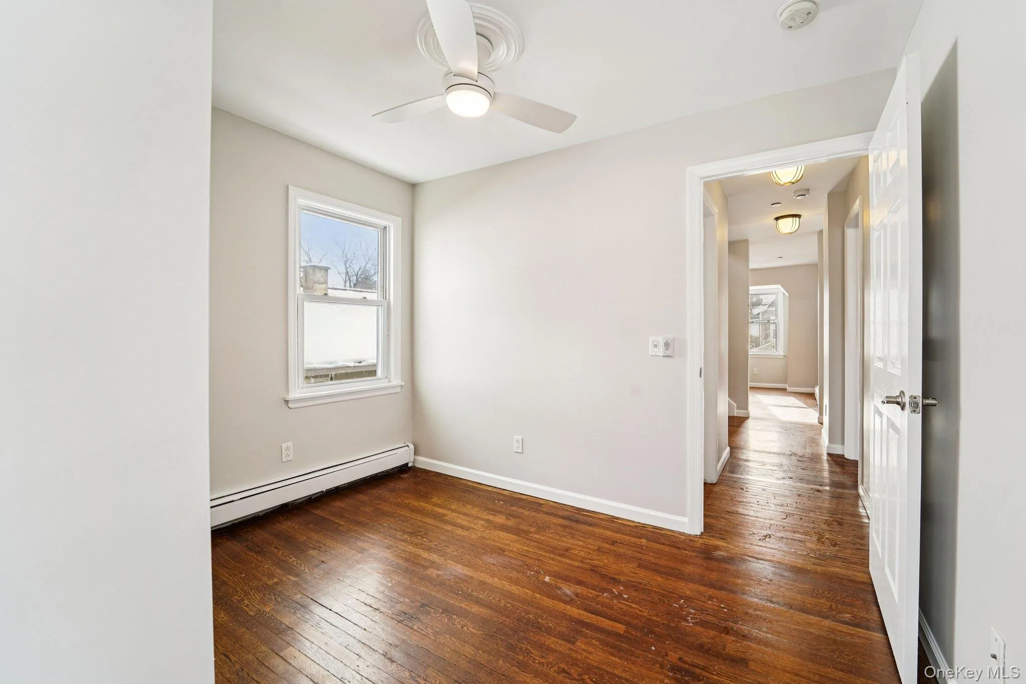 Unfurnished room featuring dark wood-style flooring, plenty of natural light, a baseboard heating unit, and a ceiling fan Unfurnished room featuring dark wood-style flooring, plenty of natural light, a baseboard heating unit, and a ceiling fan