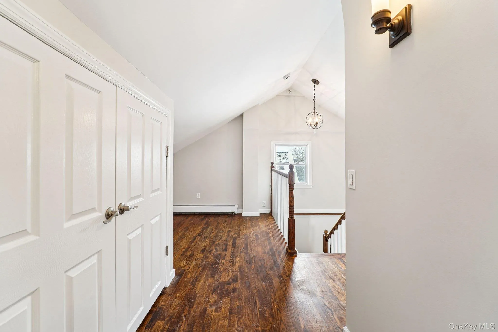 Corridor featuring an upstairs landing, dark wood-type flooring, vaulted ceiling, and a baseboard radiator Corridor featuring an upstairs landing, dark wood-type flooring, vaulted ceiling, and a baseboard radiator