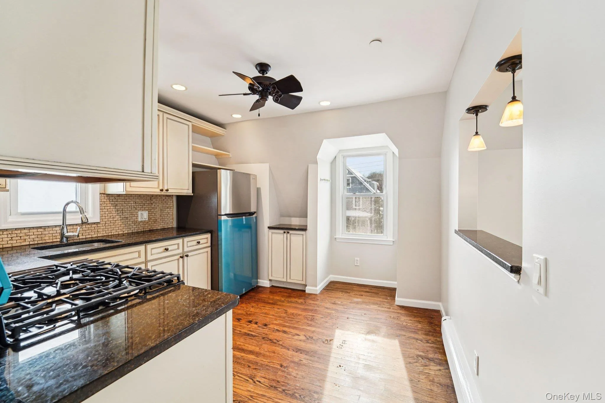 Kitchen featuring open shelves, decorative backsplash, dark stone counters, light wood finished floors, and decorative light fixtures Kitchen featuring open shelves, decorative backsplash, dark stone counters, light wood finished floors, and decorative light fixtures